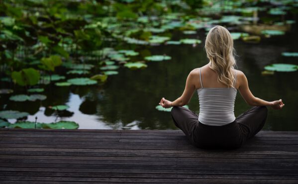 Una mujer medita junto a un estanque con flores de loto, un entorno lleno de paz para conectar con la energía emocional, espiritual y física.
